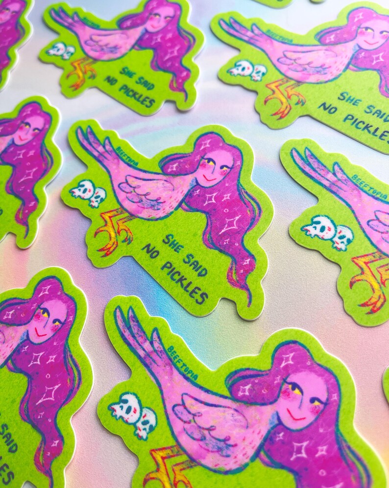 May include: A selection of stickers with a quirky design. Each sticker shows a woman with pink hair and a bird's body, set against a green background. The text "SHE SAID NO PICKLES" and "BEEFTOPIA" are included.