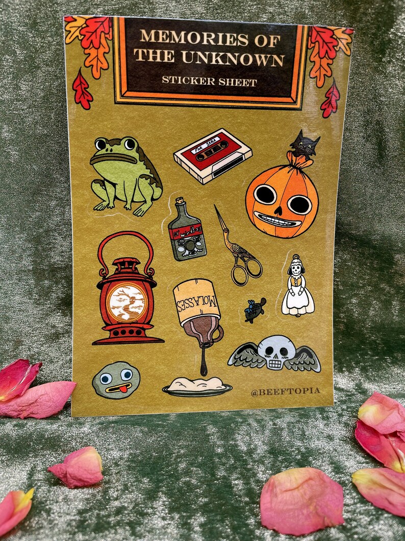 May include: A sticker sheet with a vintage book cover design featuring illustrations of a frog, a cassette tape, a jack-o-lantern, a bottle of liquor, a pair of scissors, a lantern, a bottle of molasses, a turtle, a woman in a dress, a skull with wings, and a rock with a face. The sheet is titled "Memories of the Unknown Sticker Sheet".