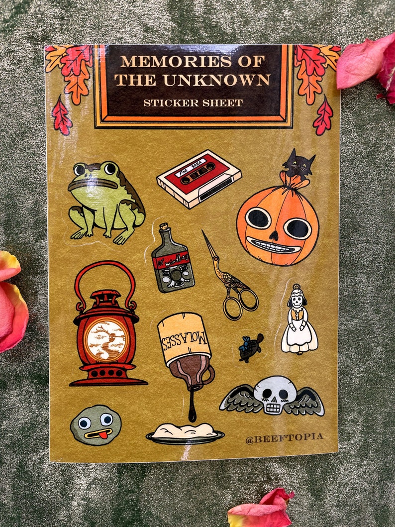 May include: A sticker sheet with a gold background featuring various illustrations, including a frog, a cassette tape, a pumpkin, a lantern, a bottle of molasses, a pair of scissors, a doll, a skull with wings, and a small round creature with a tongue sticking out. The text "Memories of the Unknown" and "Sticker Sheet" are at the top of the sheet. The text "@BEEFTOPIA" is at the bottom of the sheet.