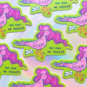 May include: A selection of stickers with a quirky design of a bird-woman with pink hair and a smiling face. The stickers have a green background and the text "SHE SAID NO PICKLES".