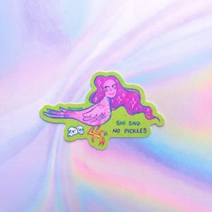 May include: A sticker depicting a fantastical bird-like figure with pink hair and a smiling face. The creature is pink and purple with yellow legs, set against a green backdrop. The text "SHE SAID NO PICKLES" is visible.