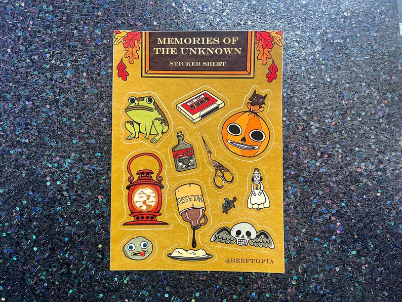 May include: A sticker sheet with a vintage aesthetic featuring various spooky and whimsical illustrations. The sheet includes a frog, a lantern, a skull with wings, a pumpkin with a toothy grin, a bottle of liquid, a cassette tape, a doll, a jar of molasses, and a small creature. The sheet is titled "Memories of the Unknown Sticker Sheet" and includes the social media handle @BEEFTOPIA.