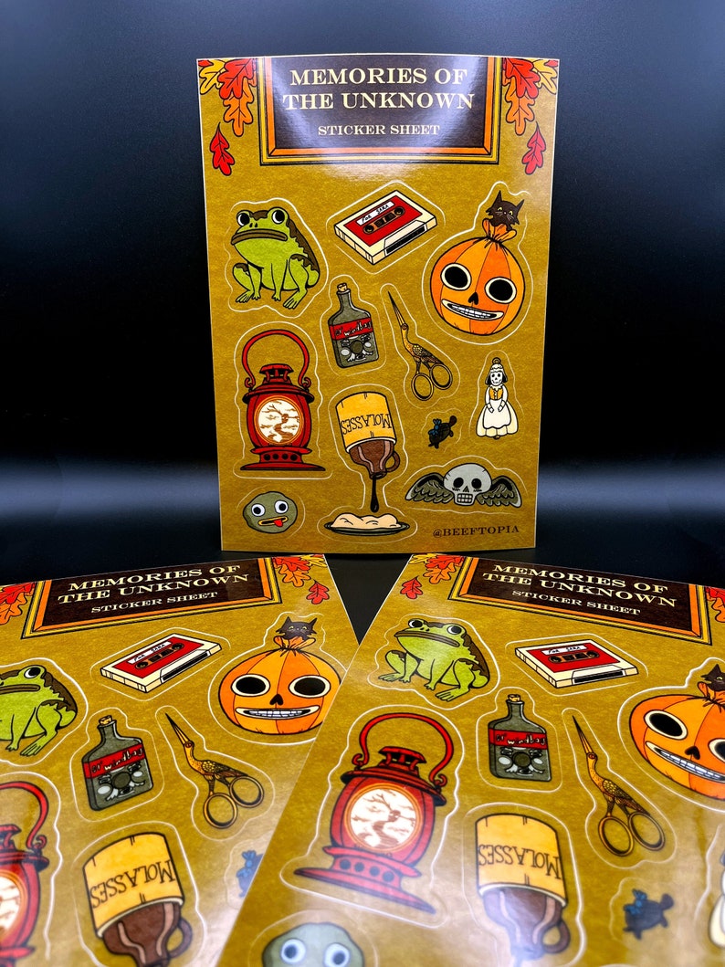 May include: A sticker sheet with a yellow background featuring various illustrations, including a frog, a lantern, a bottle, a pumpkin, a cassette tape, a pair of scissors, a bird, and a skull. The text "Memories of the Unknown" is at the top of the sheet.
