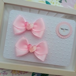May include: Two pink hair bows with glitter hearts. The bows are displayed on a white background with pink polka dots. The text "Bee Maru" is on a pink circle.
