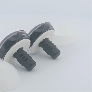 May include: Two black and clear plastic doll eyes with white foam bases and black screw posts. The eyes are glossy and have a reflective quality. The background is plain white.