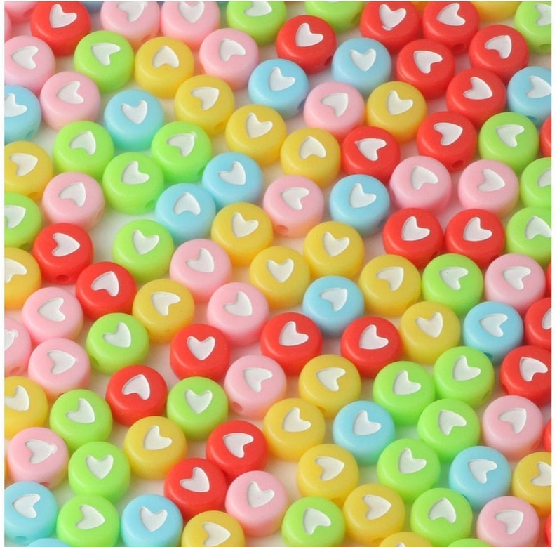 Puede incluir: Una colecci&oacute;n de cuentas redondas y coloridas en varios tonos de rosa, rojo, amarillo, verde y azul. Cada cuenta tiene un dise&ntilde;o en forma de coraz&oacute;n blanco en el centro. Estas cuentas probablemente se utilizan para hacer joyas o proyectos de manualidades.