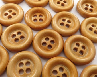 May include: A collection of light brown wooden buttons with four holes each. The buttons are round with a slightly raised center and a smooth, polished finish. The buttons are arranged closely together.