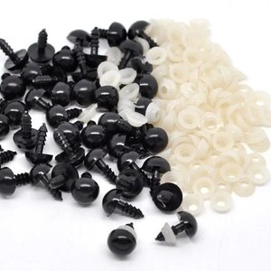 Op de afbeelding: Een verzameling zwarte plastic veiligheidsoogjes met schroefdoppen en witte plastic ringen. Deze knutselbenodigdheden worden gebruikt voor het maken van knuffels, poppen en andere handgemaakte projecten. De ogen zijn glanzend en rond.