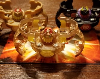 Könnte beinhalten: Drei transparente Spielzeugfiguren aus Kunststoff in Gold- und Rottönen. Die Figuren haben die Form einer Spinne mit einem runden Kopf und mehreren Beinen. Die Figuren befinden sich auf einem roten und orangenen Hintergrund.