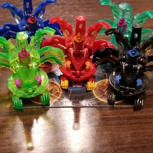 May include: Four colorful toy figures with multiple arms and legs. The figures are made of translucent plastic and have a variety of colors, including blue, green, red, and black.