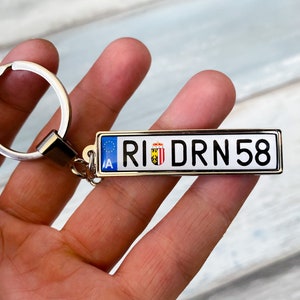 Può includere: Un portachiavi argentato con un ciondolo a forma di targa blu, bianca e gialla che dice "RIDRN 58".
