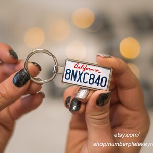 May include: A silver keychain with a white California license plate featuring the text "California" and the license plate number "8NXC840".