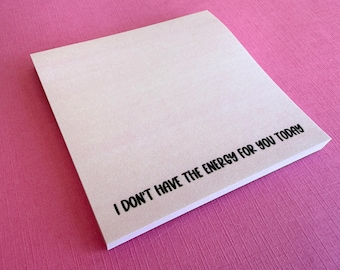 May include: A square notepad with light gray paper featuring the black printed text I DON'T HAVE THE ENERGY FOR YOU TODAY positioned along the bottom right corner of the top sheet. The notepad consists of multiple stacked sheets of paper.