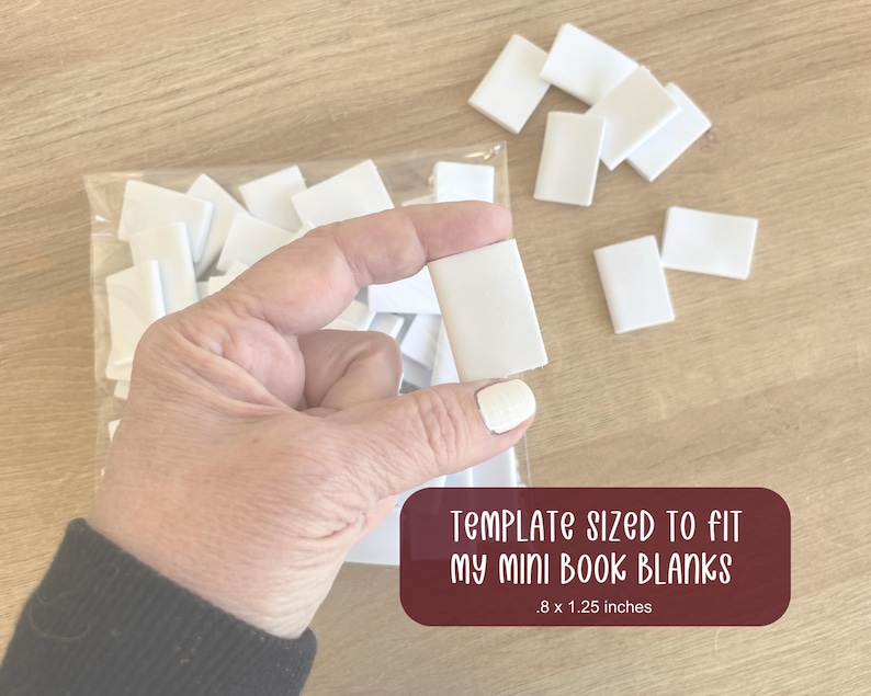Puede incluir: Una mano sostiene un peque&ntilde;o libro en blanco rectangular blanco. Los libros en blanco est&aacute;n en una bolsa de pl&aacute;stico transparente y esparcidos sobre una superficie de madera. El texto en una etiqueta granate dice "TEMPLATE SIZED TO FIT MY MINI BOOK BLANKS .8 x 1.25 inches" (aproximadamente 2 x 3 cm).