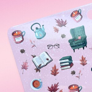 May include: A pink sticker sheet with fall-themed illustrations. The sheet features images of a teal teapot, a green armchair, burning candles in mugs, open books, fall leaves, and eyeglasses. The illustrations are in a watercolor style.
