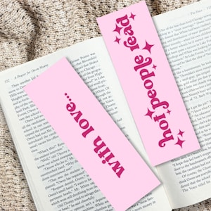 May include: Two rectangular light pink bookmarks featuring dark pink text. One bookmark displays the words hot people read with four-pointed star icons. The second bookmark features the text with love... in a bold, stylized dark pink font.