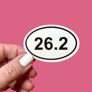 May include: An oval-shaped sticker with a white background and a thick black border. The number 26.2 is printed in the center in a bold, black, sans-serif font. The sticker has a smooth, matte finish and a clean, simple design.