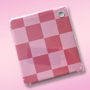 May include: A pink and red checkered tablet case with a clear, protective border. The case has a power button on the top right corner. The design features a checkerboard pattern with a glittery effect.