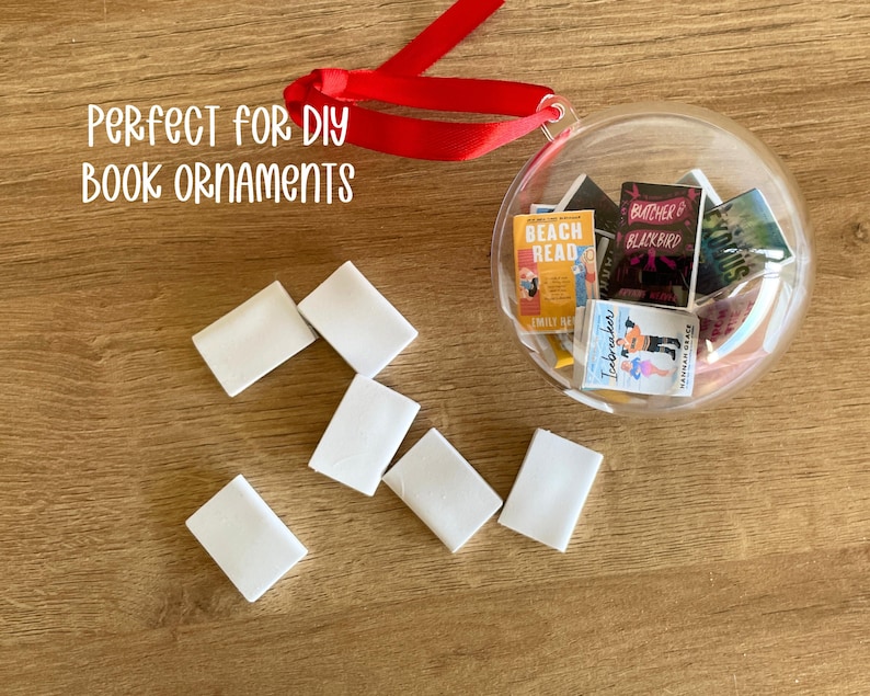 Puede incluir: Una bola transparente llena de r&eacute;plicas de libros en miniatura, con una cinta roja para colgar. Varios bloques rectangulares blancos est&aacute;n dispersos alrededor de la bola. El texto "PERFECT FOR DIY BOOK ORNAMENTS" es visible.