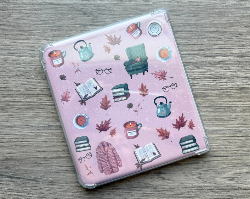 May include: A clear tablet case with a pink background featuring illustrations of autumn-themed items. The design includes a green armchair, books, eyeglasses, candles, teacups, a teapot, and fall leaves.