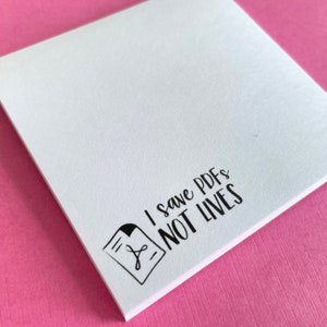 May include: A square white sticky note featuring a black graphic of a document icon with a PDF symbol and the black text that reads I save PDFs NOT LIVES printed in a stylized font on the bottom left corner of the paper sheet.