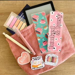 May include: A pink corduroy pouch with a variety of book-themed bookmarks and stickers. The bookmarks feature illustrations of books, coffee cups, and flowers. The stickers include the text "BOOKS", "An Annotated Book is a Well-Loved Book", and "There's No Such Thing as Too Many Books".