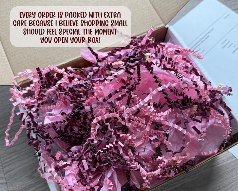 May include: An open cardboard shipping box filled with crinkled paper filler in shades of light pink and dark burgundy. A white text box overlay reads: EVERY ORDER IS PACKED WITH EXTRA CARE BECAUSE I BELIEVE SHOPPING SMALL SHOULD FEEL SPECIAL THE MOMENT YOU OPEN YOUR BOX!