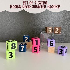 May include: A set of wooden blocks labeled SET OF 2 EXTRA BOOKS READ COUNTER BLOCKS. The cubes feature various colors including lime green, navy blue, hot pink, lavender, and brown, each printed with black numbers on their faces.
