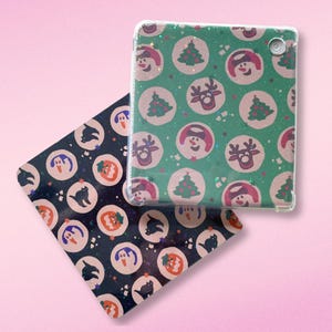 May include: Two decorative Christmas-themed items. One is a clear tablet case with a green background and repeating circles with images of snowmen, reindeer, and Christmas trees. The other is a square coaster with a navy blue background and repeating circles with images of penguins, cats, and pumpkins.