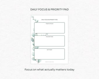 May include: A white Daily Focus & Priority Pad with three rectangular sections labeled "Today's Focus", "The One Thing", and "Not Today". The pad is decorated with watercolor eucalyptus leaves and the text "Focus on what actually matters today".