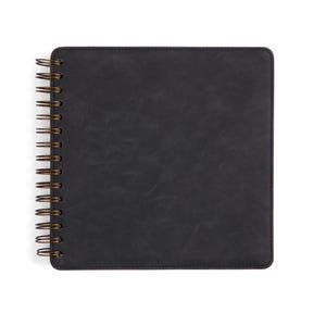May include: A black spiral bound notebook with a textured cover.