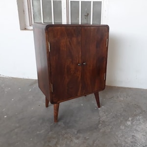 May include: A dark brown wooden cabinet with two doors and four legs. The cabinet has a simple design and is made of solid wood.