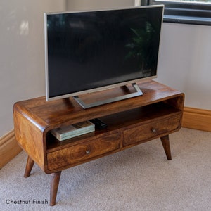 May include: A wooden TV stand with two drawers and a shelf. The stand has a chestnut finish and a curved front. A flat screen TV is sitting on top of the stand.