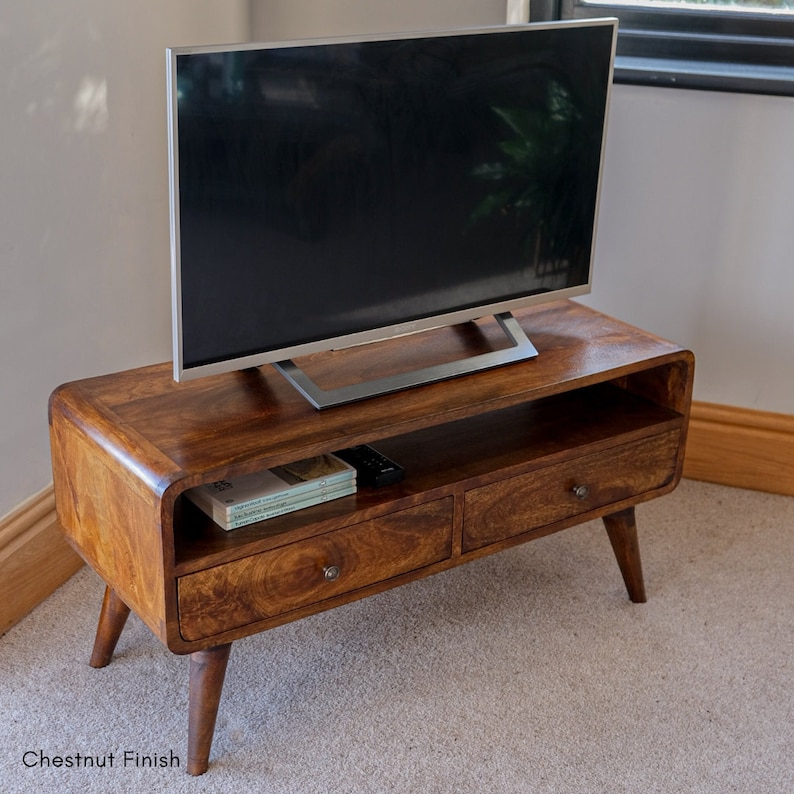 May include: A wooden TV stand with two drawers and a shelf. The stand has a chestnut finish and a curved front. A flat screen TV is sitting on top of the stand.