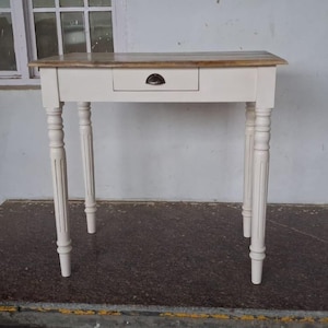 May include: A small, white wooden table with a natural wood top and a single drawer. The table has four turned legs and a dark metal drawer pull. The table is approximately 76 cm long, 46 cm wide, and 76 cm tall.