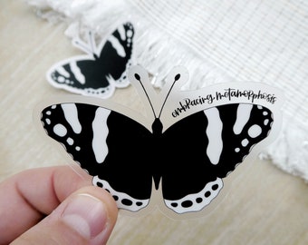 May include: Clear sticker of a black and white butterfly with the text "embracing metamorphosis" on the right wing.
