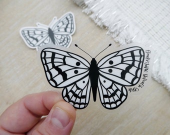 May include: A clear sticker with a black and white butterfly design. The sticker says "Simple Flourishing Through the Power".