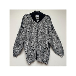 May include: A long-sleeved button-down cardigan featuring a black and white animal print pattern. The garment has a solid black ribbed collar and matching black trim along the button placket. The cuffs are also ribbed in a solid black color.