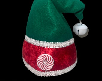 May include: Green and red felt elf hat with a white candy cane design and a white bell.