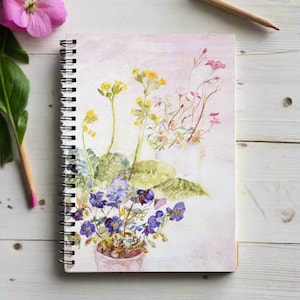 Puede incluir: Una pintura de acuarela de un ramo de flores en una maceta. Las flores son amarillas, rosas y moradas. El fondo es rosa claro.
