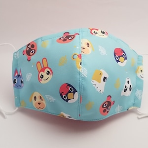 May include: A light blue face mask with a repeating pattern of animal characters from the Animal Crossing video game series. The characters include a cat, a dog, a bird, a squirrel, and a rabbit. The mask has white elastic straps.