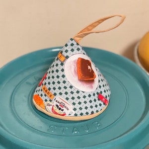 May include: A green and white patterned fabric cone-shaped pouch with a handle. The pouch has a printed image of a slice of cake and the text "Black & White" and "Black Tea".