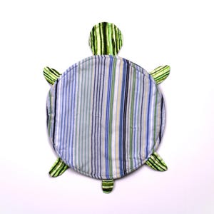 May include: A fabric turtle-shaped mat featuring a circular shell with vertical blue, white, and green stripes. The head and four flippers are made from a green and black striped fabric. The entire piece is quilted with visible stitching lines.