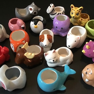 May include: A collection of sixteen small ceramic animal-shaped planters featuring a variety of creatures including a raccoon, zebra, leopard, flamingo, penguin, octopus, turtle, seal, fox, dog, polar bear, crab, moose, cat, dinosaur, elephant, whale, and walrus.