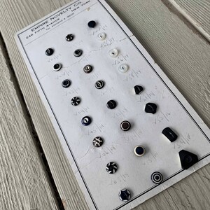 May include: A white card with black and white buttons arranged in rows. The card has the text "EMPIRE NOVELTY CO. 246 FIFTH AVENUE NEW YORK Tel. Ashland 4-9600" printed on it. Each button has a handwritten number next to it.
