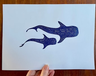 May include: A blue and white print of two whale sharks swimming. The larger whale shark is in front of the smaller whale shark. The print is on white paper.