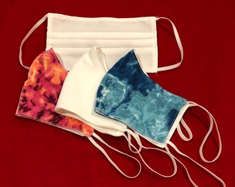 May include: Three fabric face masks with elastic ear loops. One mask is white, one is pink with orange and white swirls, and one is blue with white swirls.