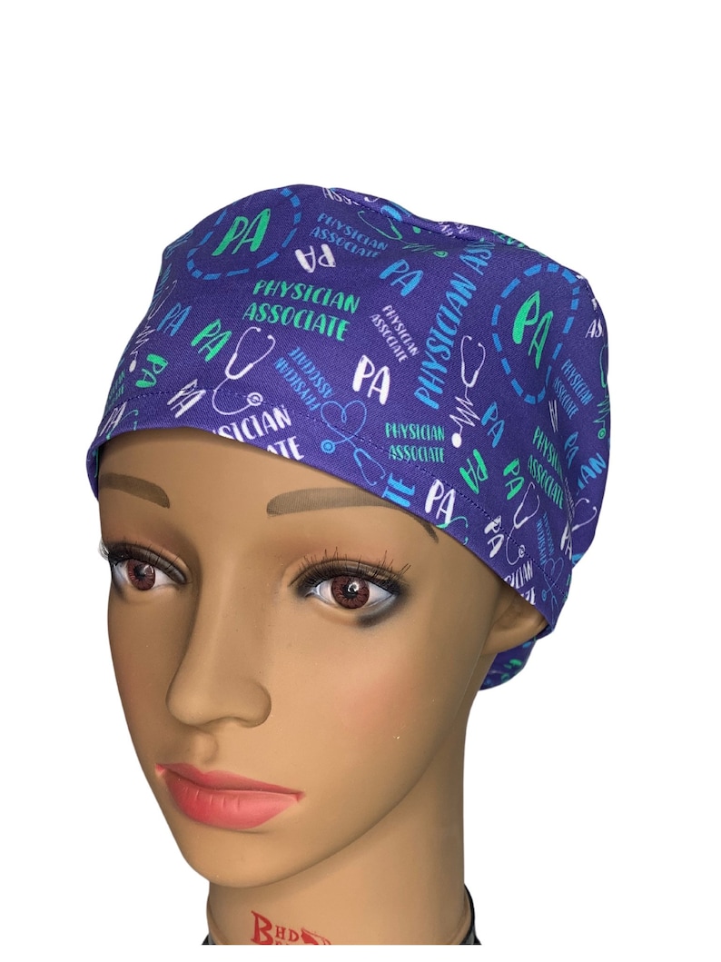 May include: Purple scrub hat with a repeating pattern of the words "Physician Associate" and "PA" in green and white text. A stethoscope is also included in the pattern.