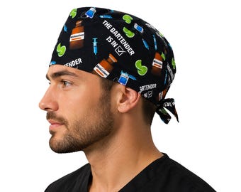 May include: A black scrub cap featuring a repeating pattern of brown medicine bottles labeled Midazolam, blue syringes, and green lime slices. The text THE BARTENDER IS IN with a checkmark is printed in white across the fabric of the head covering.