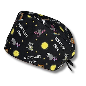 Puede incluir: Un gorro de quirófano negro con un patrón repetido de mapaches, murciélagos, búhos, lunas, estrellas y jeringas. El texto "Night Shift Crew" se repite en todo el patrón.